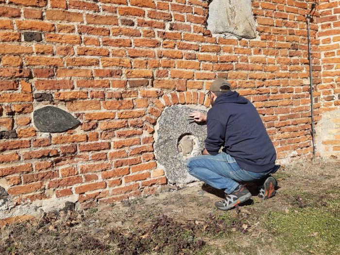 Dr. Maciej Prarat (UMK în Toruń) prelevând mostre de mortar în jurul unei pietre de moară pentru analize de laborator ulterioare (Fotografia de Dariusz Brykała)