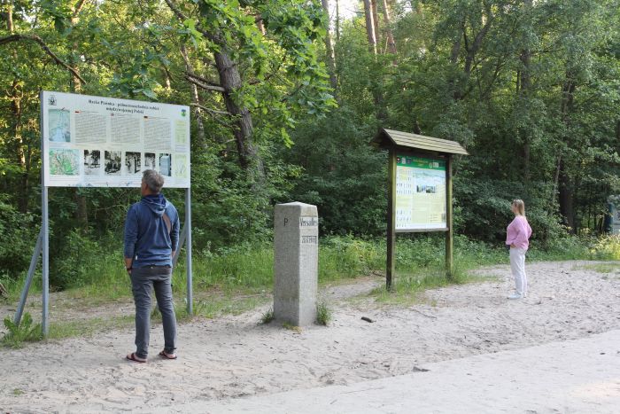 Turyści oglądający międzywojenny słup wersalski wraz z tablicami informacyjnymi (Dębki; dawna granica pomiędzy Polską a Niemcami)