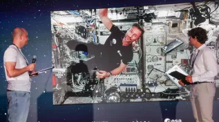 Łódź, 02.07.2025. Przebywający na Międzynarodowej Stacji Kosmicznej polski astronauta Sławosz Uznański-Wiśniewski (na ekranie) podczas połączenia wideo na żywo w EC1 w Łodzi, 2 bm. Podczas trwającego ok. 20 minut połączenia Sławosz Uznański-Wiśniewski wykonywał eksperymenty w stanie nieważkości oraz odpowiadał na pytania zadawane przez młodzież. (jm) PAP/Marian Zubrzycki