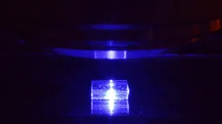 Pobudzany światłem niebieskim kryształ fluorku litu z zarejestrowanymi śladami cząstek jonizujących podczas obserwacji pod mikroskopem fluorescencyjnym. (Źródło: IFJ PAN)