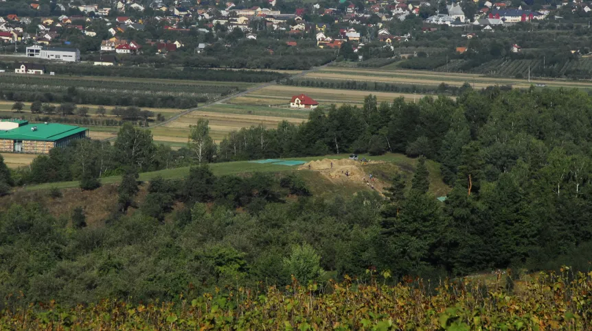 Widok na strefę prac archeologicznych na „Górze Zyndrama” w Maszkowicach, w tle panorama Łącka. Łatwo dostrzec sztuczne wypłaszczenie szczytu i stromiznę na wschodnim stoku, kryjącą kamienne fortyfikacje z epoki brązu. Fot. A. Maślak. 