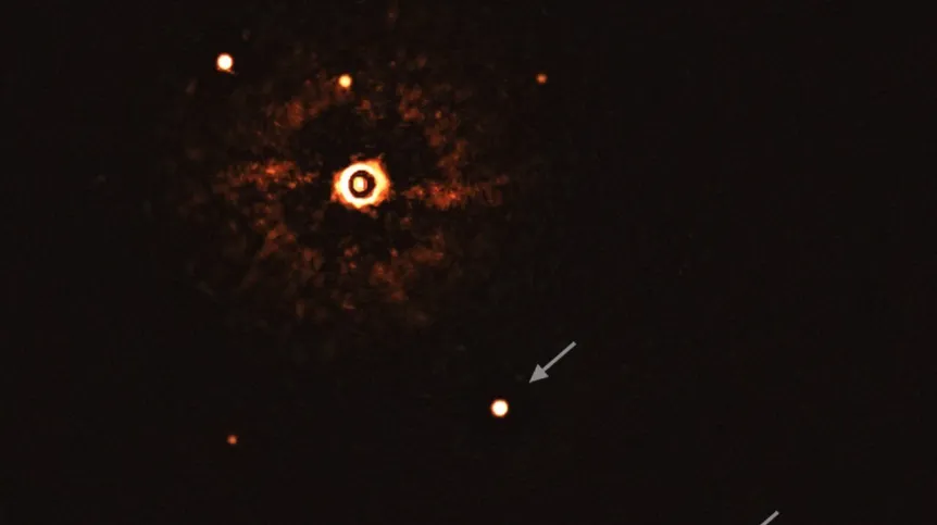 Zdjęcie uzyskane przez instrument SPHERE na należącym do ESO teleskopie VLT pokazuje gwiazdę TYC 8998-760-1 wraz z towarzyszącymi jej dwoma olbrzymimi egzoplanetami. Planety są widoczne jako jasne plamki w centrum (TYC 8998-760-1b) i w prawym dolnym rogu (TYC 8998-760-1c) obrazu. Wskazano je strzałkami. Inne jasne plamki to gwiazdy tła. Dzięki wykonaniu zdjęć w różnym czasie naukowcy byli w stanie odróżnić planety od gwiazd tła. Źródło: ESO/Bohn et al.