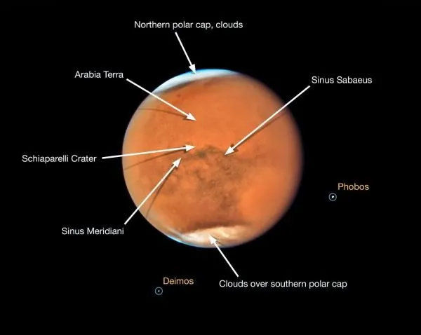 Zdjęcie Marsa blisko opozycji wykonane 18 lipca 2018 r. przez Kosmiczny Teleskop Hubble’a. Zaznaczono różne struktury na powierzchni planety. Na zdjęciu widać także dwa księżyce planety. Źródło: NASA, ESA, STScI.